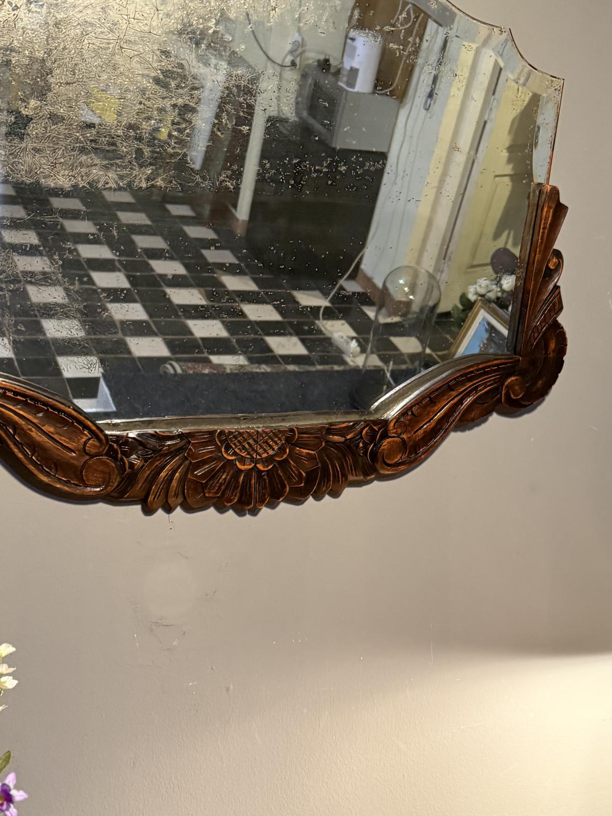 Oglindă veche de 78 × 54 cm, cu ramă sculptată din lemn și patină accentuată pe suprafața oglinzii. Rama a fost reparată.