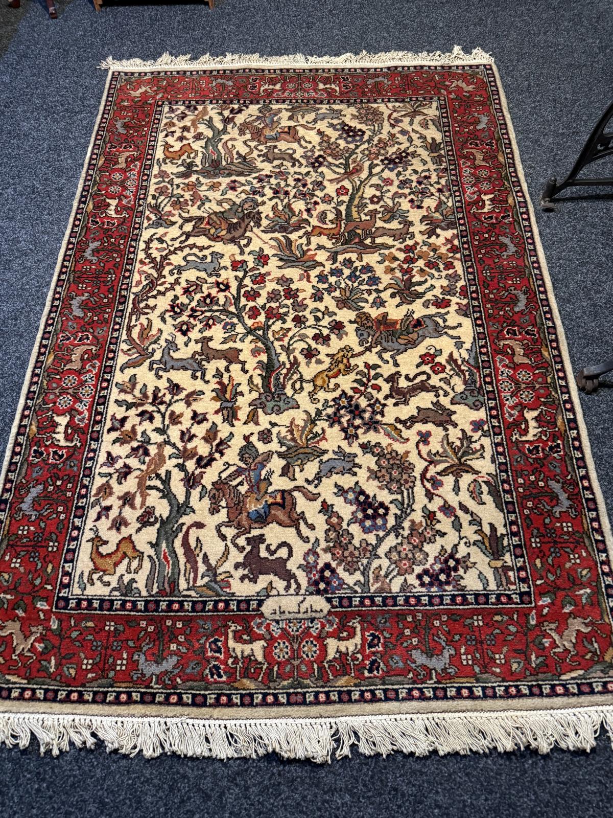 Covor persan vechi lucrat manual, cu scenă de vânătoare, călăreți și animale, păstrat suspendat pe perete. Dimensiuni 200 × 130 cm.