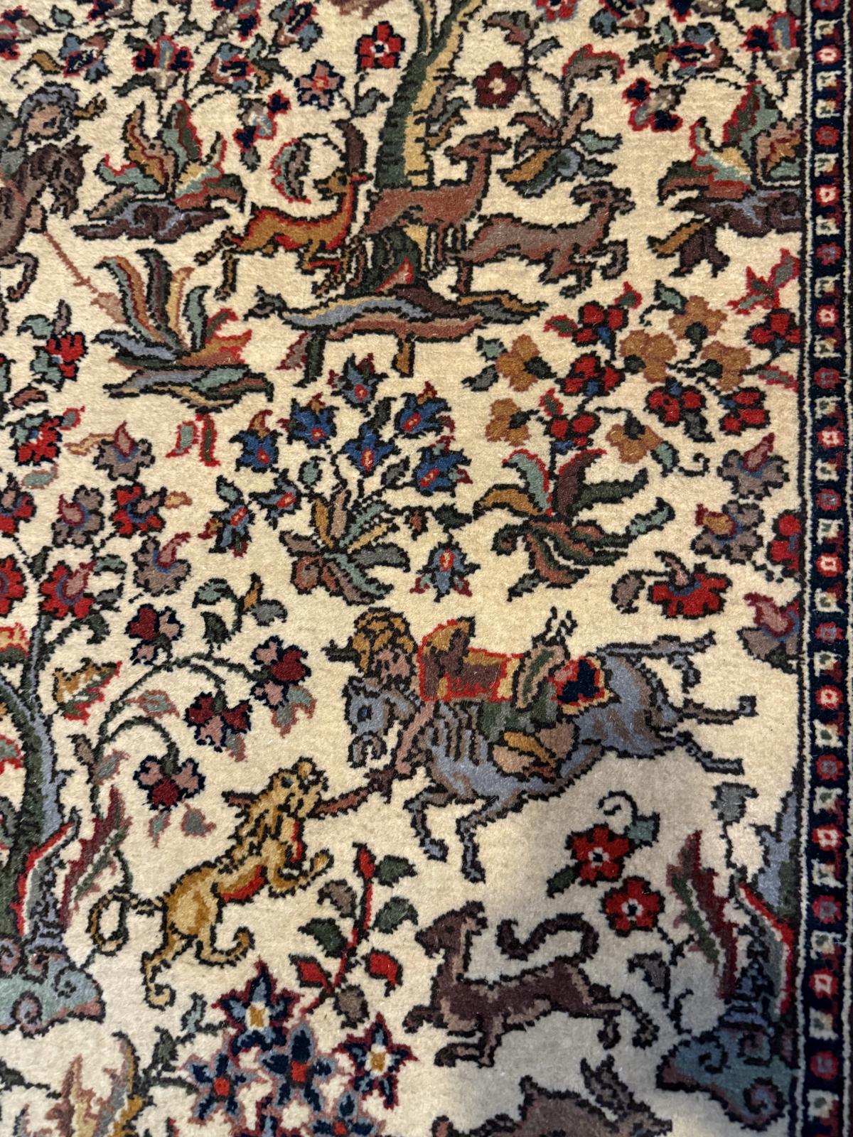Covor persan vechi lucrat manual, cu scenă de vânătoare, călăreți și animale, păstrat suspendat pe perete. Dimensiuni 200 × 130 cm.
