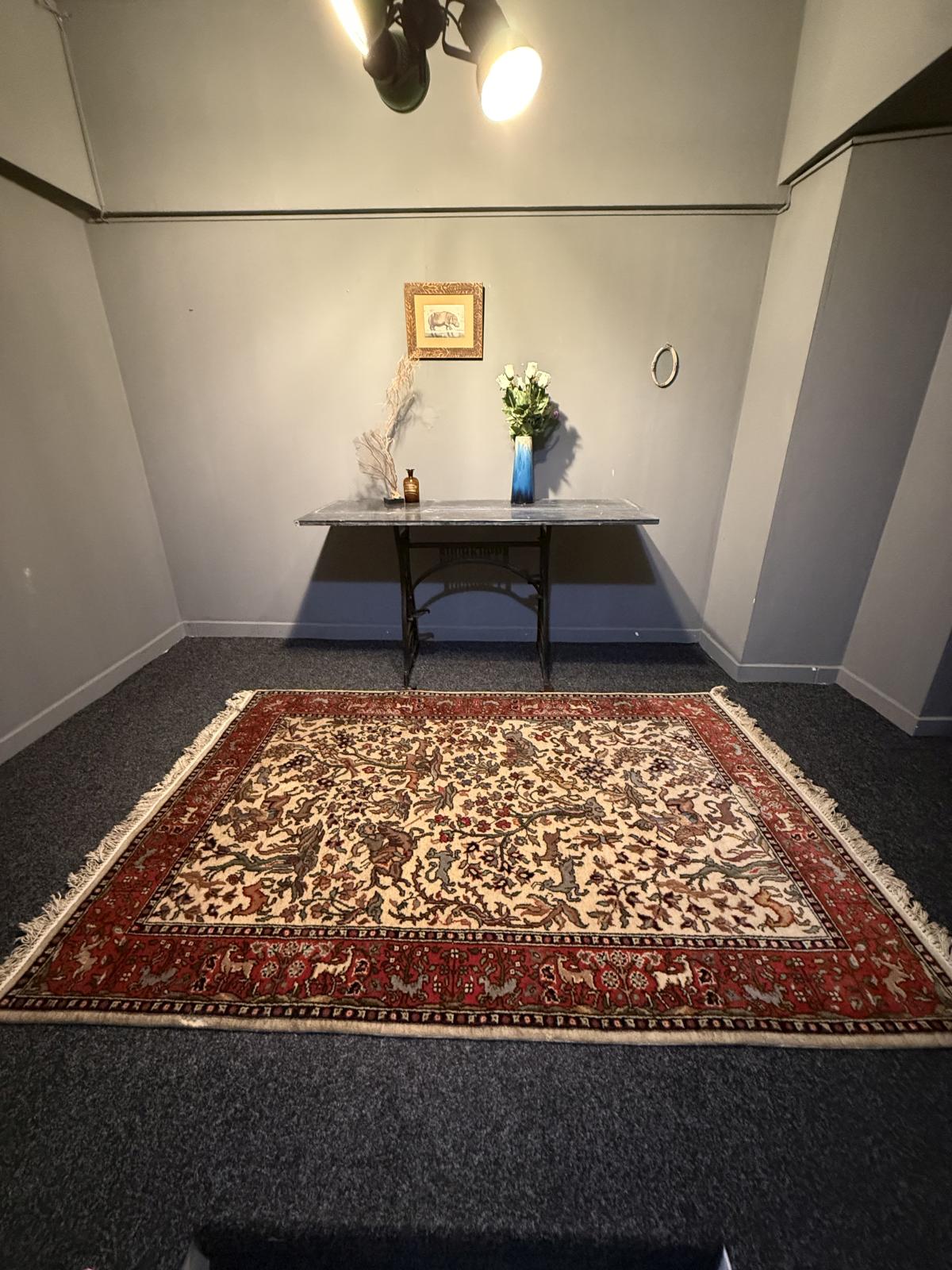 Covor persan vechi lucrat manual, cu scenă de vânătoare, călăreți și animale, păstrat suspendat pe perete. Dimensiuni 200 × 130 cm.