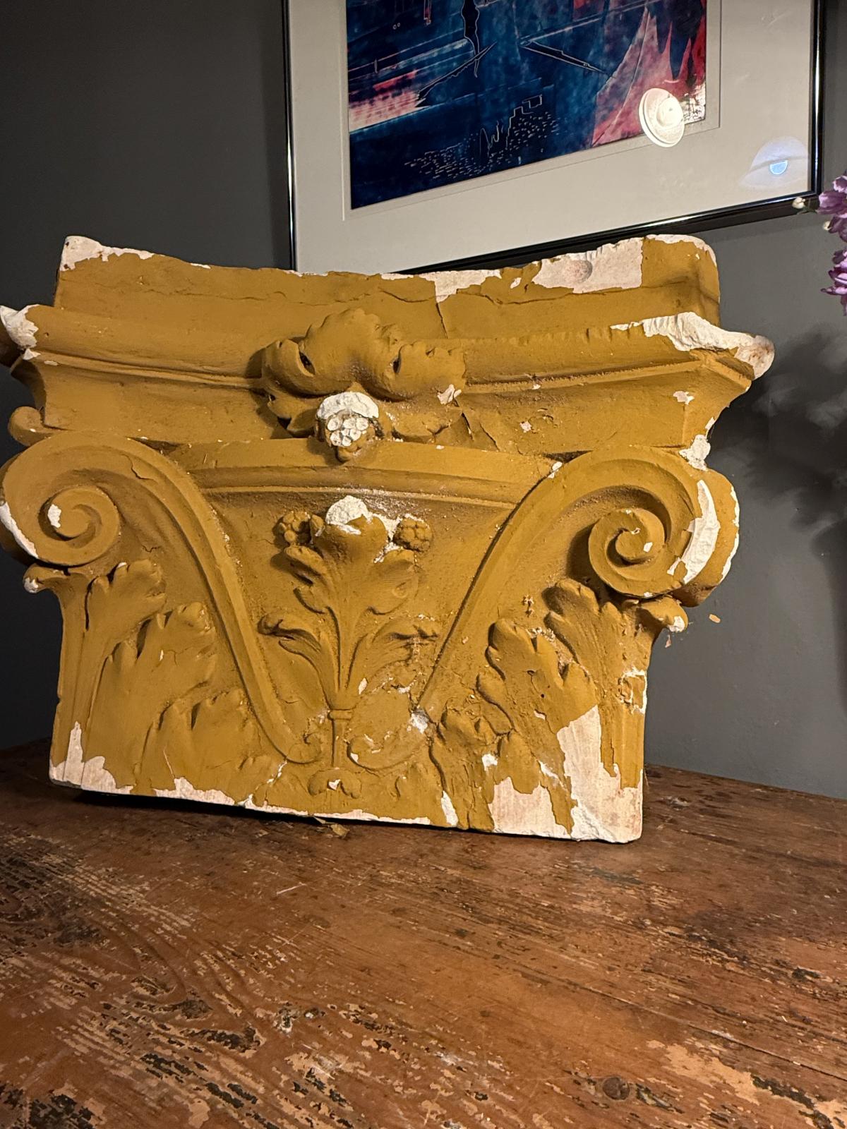 Capitel decorativ din ipsos, cu volute și frunze de acant în relief. Patină ocru, urme de uzură și ciobituri. Dimensiuni: 55 × 40 × 19 cm.