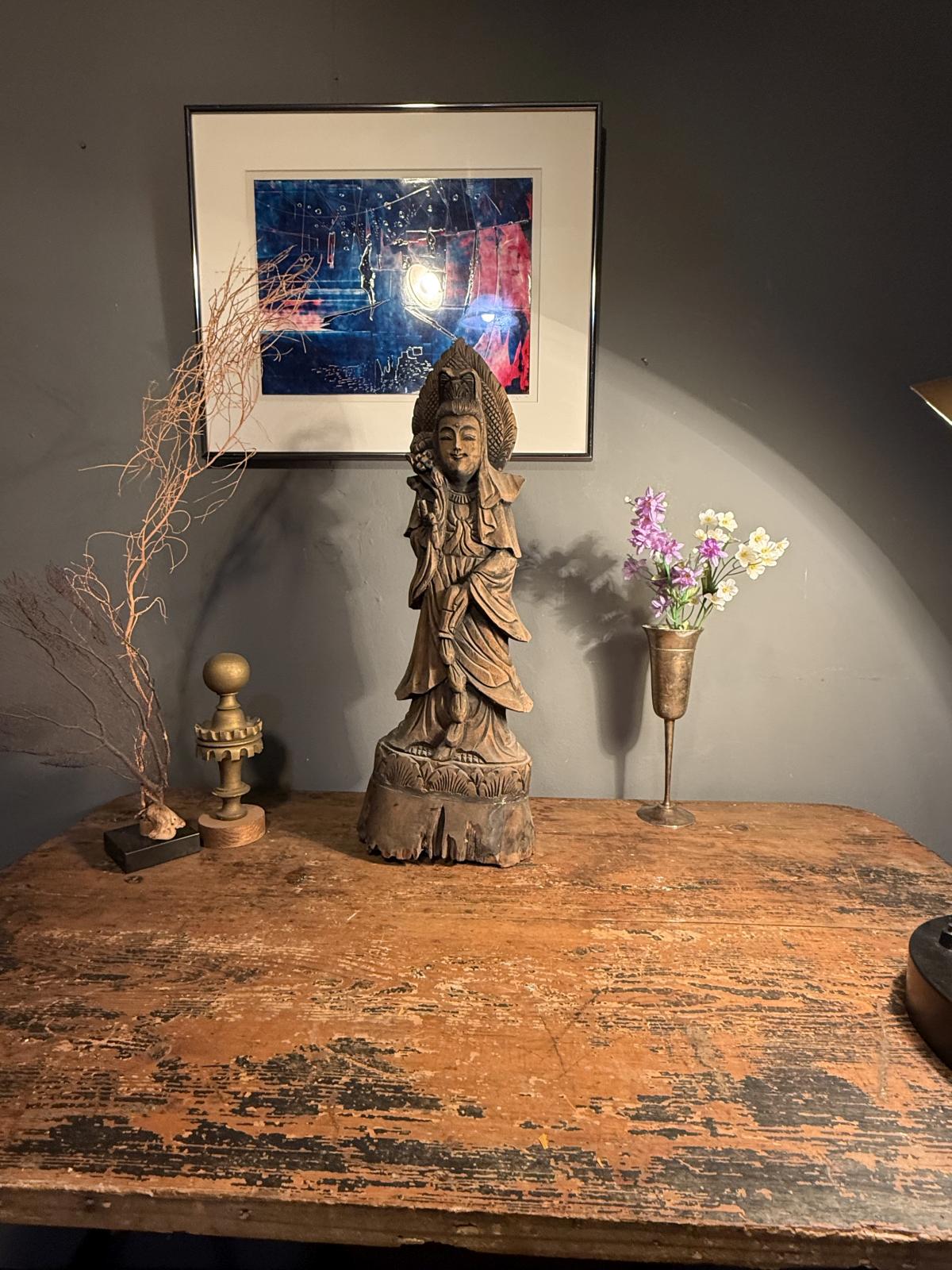 Statuetă orientală din lemn sculptat, cu veșminte drapate și patină brună. Înălțime 55 cm. Prezintă fisuri și lipsuri de material la bază.