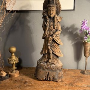 Statuetă orientală din lemn sculptat, cu veșminte drapate și patină brună. Înălțime 55 cm. Prezintă fisuri și lipsuri de material la bază.
