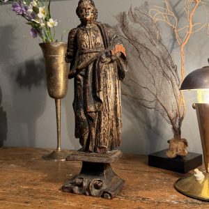 Statuetă religioasă din lemn sculptat, atribuită secolului XVIII, cu urme de policromie și soclu cu volute. Înălțime 28 cm, cu lipsuri.