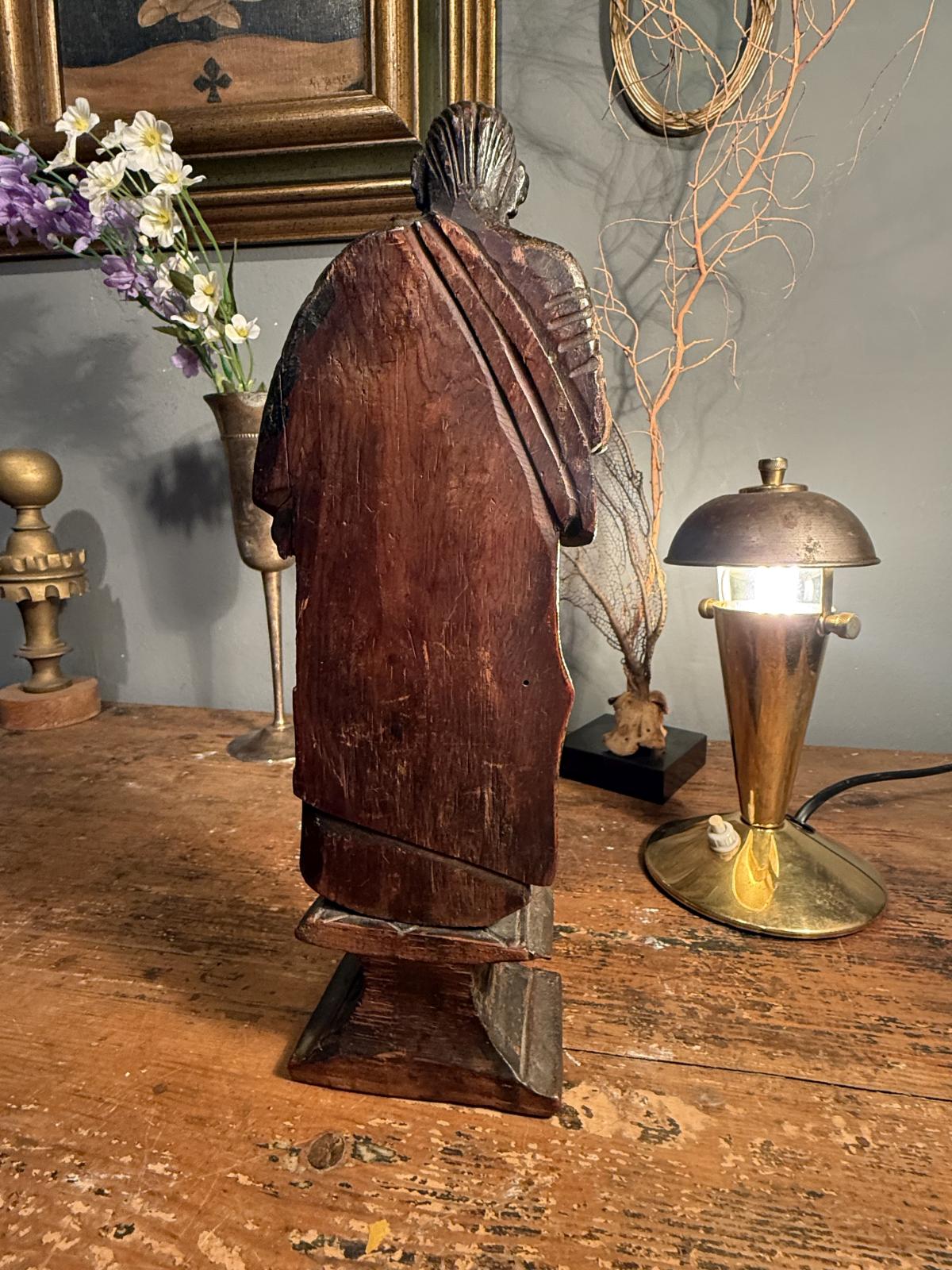 Statuetă religioasă din lemn sculptat, atribuită secolului XVIII, cu urme de policromie și soclu cu volute. Înălțime 28 cm, cu lipsuri.