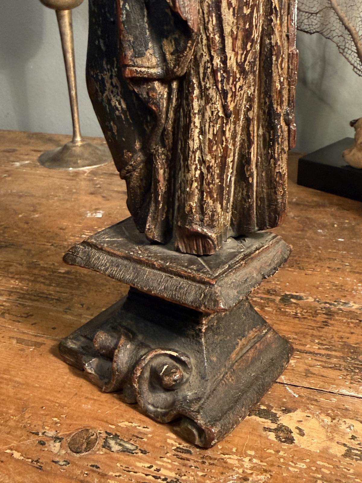 Statuetă religioasă din lemn sculptat, atribuită secolului XVIII, cu urme de policromie și soclu cu volute. Înălțime 28 cm, cu lipsuri.