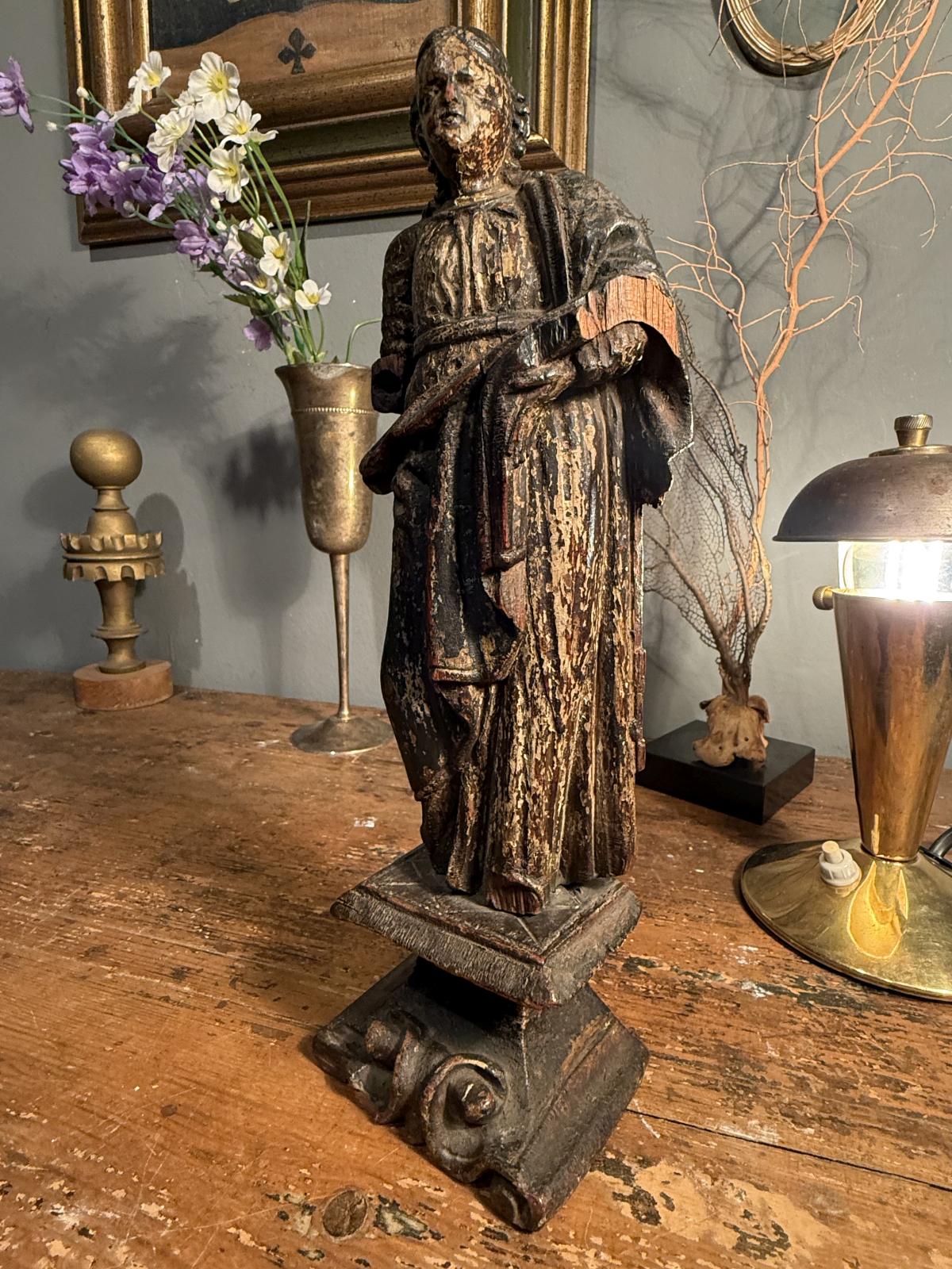Statuetă religioasă din lemn sculptat, atribuită secolului XVIII, cu urme de policromie și soclu cu volute. Înălțime 28 cm, cu lipsuri.